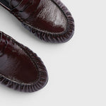 JONES + CO Sydney wine crinkle patent leather penny loafers with ruched detailing, top-down view.