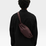 JONES + CO Bon-Bon M wine leather crossbody bag worn by a person in a black jacket