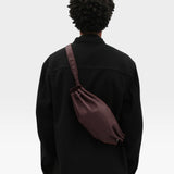 JONES + CO Bon-Bon M wine leather crossbody bag worn by a person in a black jacket
