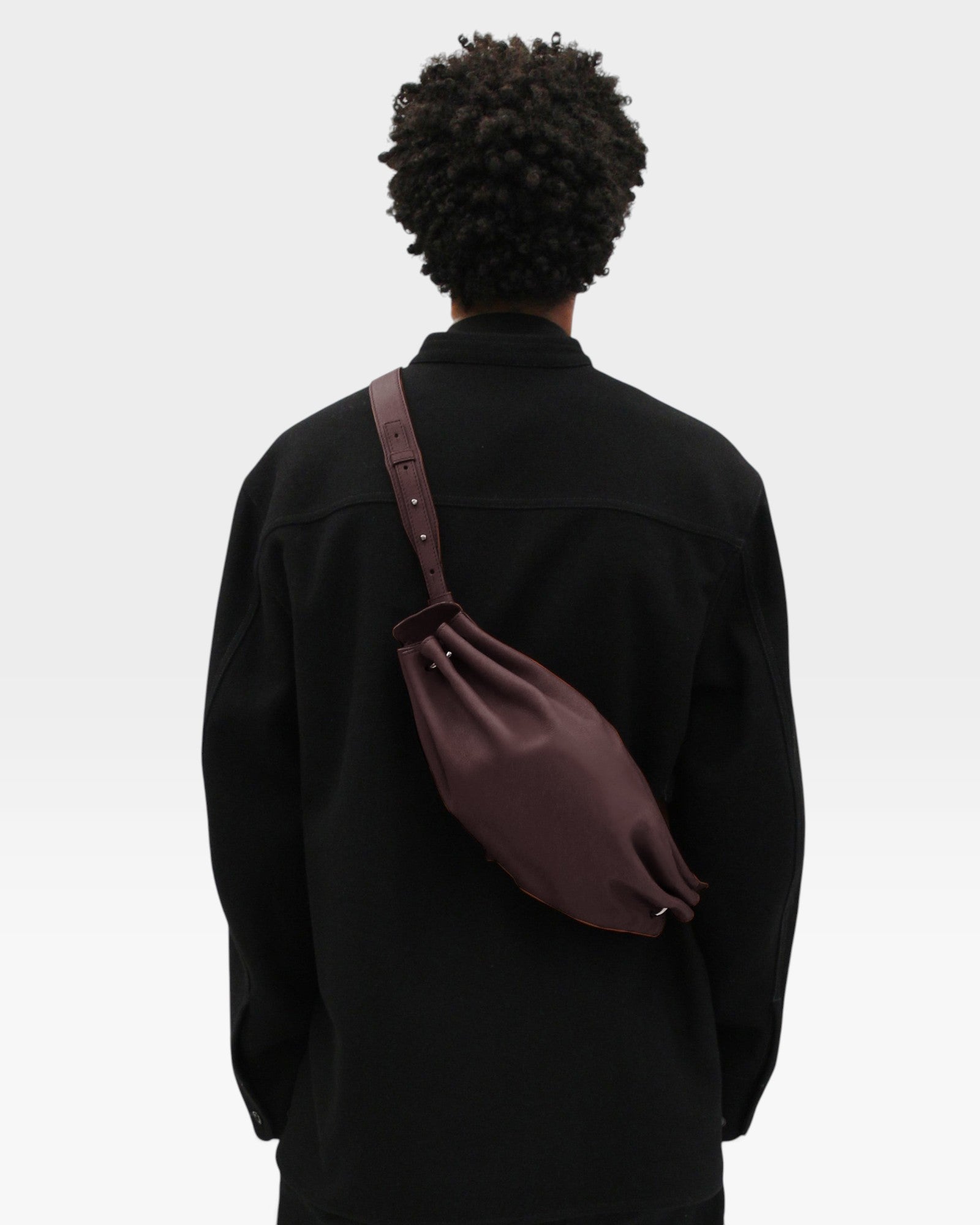 JONES + CO Bon-Bon M wine leather crossbody bag worn by a person in a black jacket