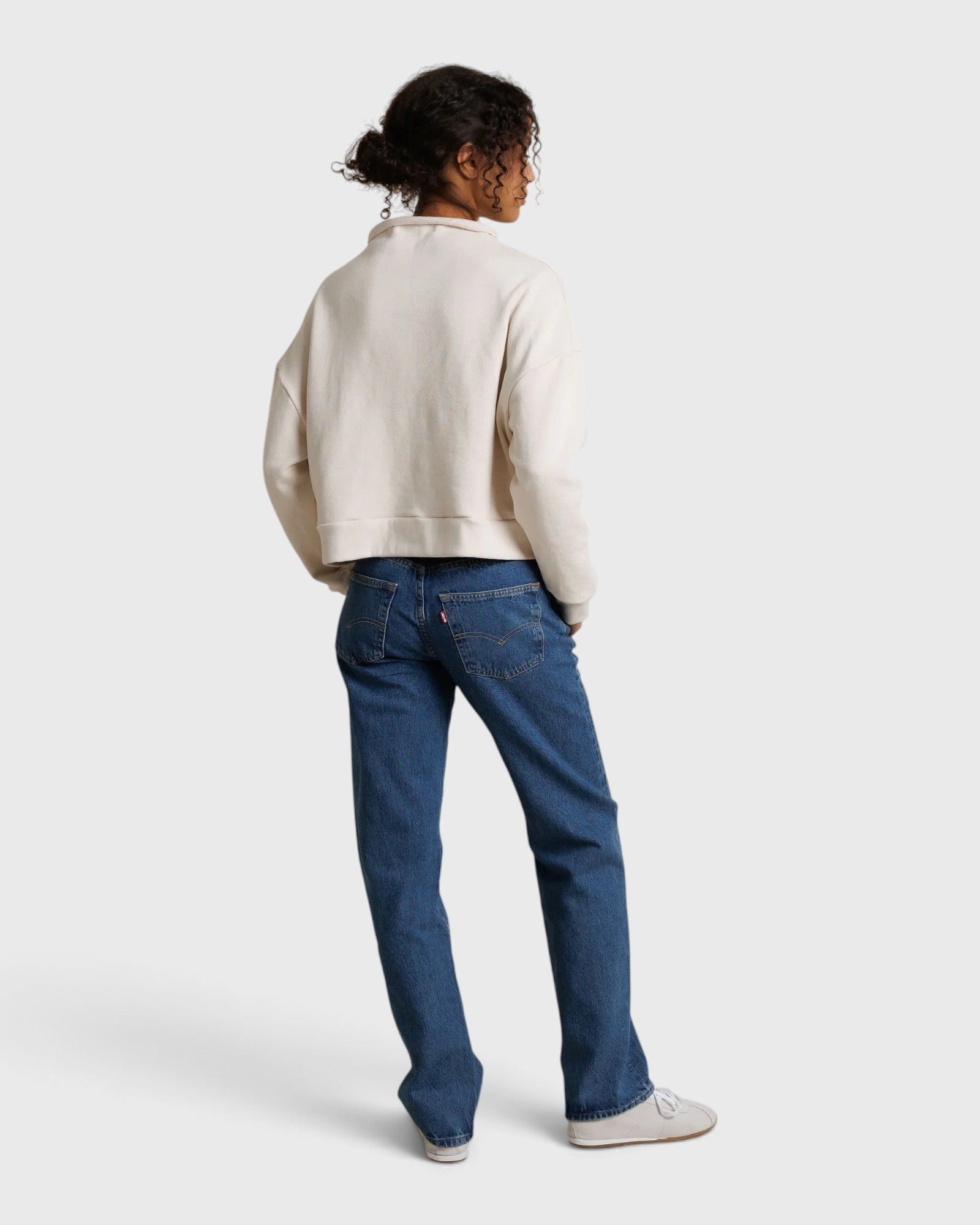 Model wearing JONES + CO Arden mock neck sweatshirt in sugar French terry with blue denim jeans, back view