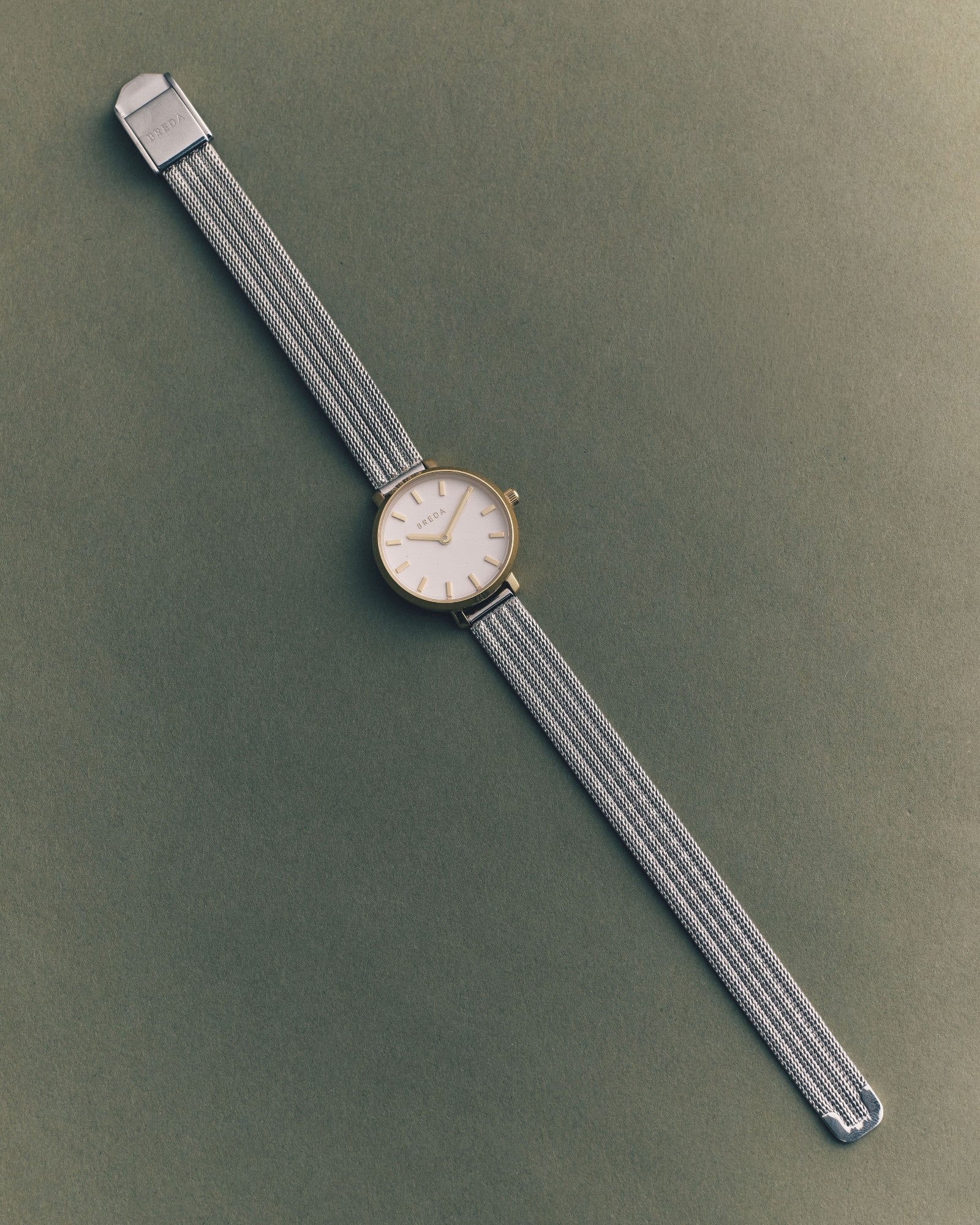 JONES + CO Beverly mesh watch in silver with a round white dial and minimalist markers on a dark green background.