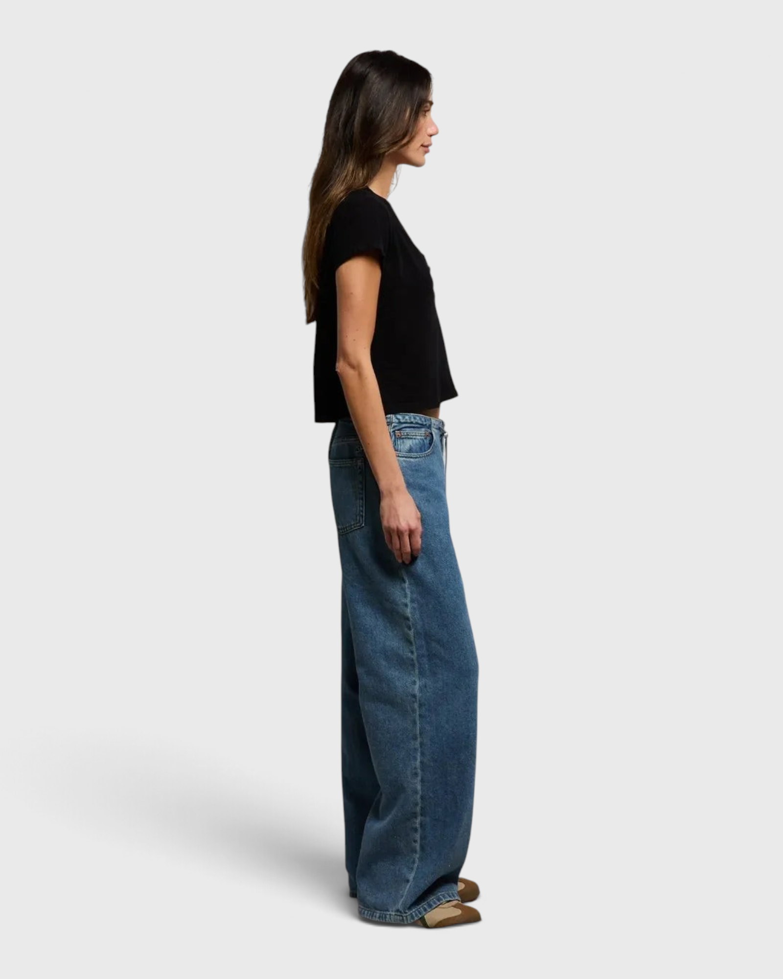 Model wearing JONES + CO black recycled cotton cropped V-neck t-shirt with wide-leg jeans, side profile view.