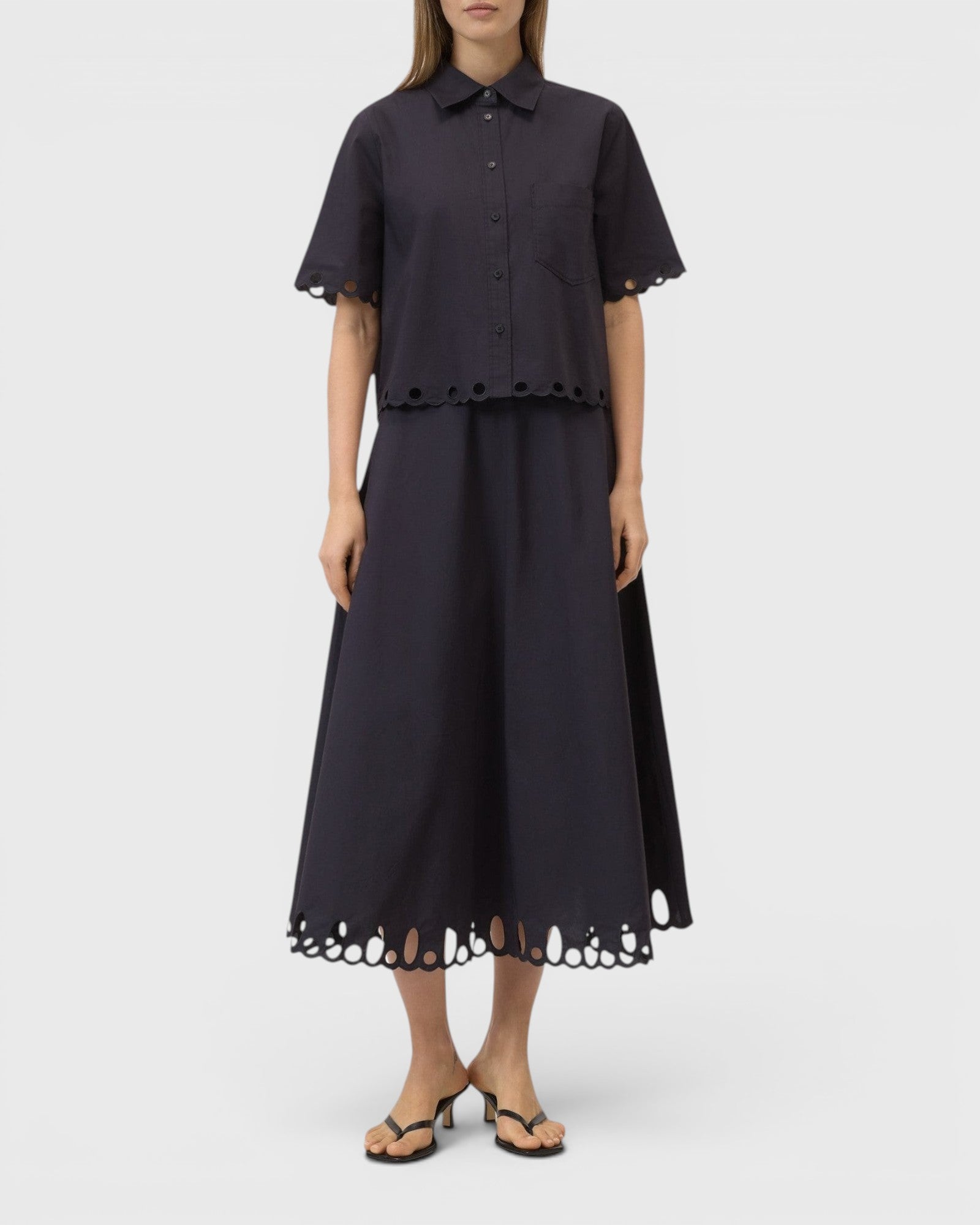 JONES + CO black midi skirt with flared silhouette and intricate cut-out embroidery along the hem on a model.