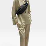 JONES + CO Bon-Bon M black leather crossbody bag with metal clasp worn by a model in a beige silk shirt and trousers