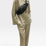 JONES + CO Bon-Bon M black leather crossbody bag with metal clasp worn by a model in a beige silk shirt and trousers