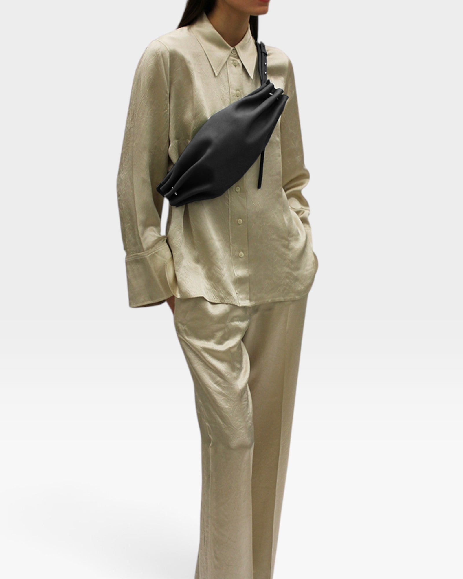 JONES + CO Bon-Bon M black leather crossbody bag with metal clasp worn by a model in a beige silk shirt and trousers