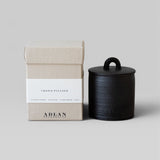 JONES + CO Crowd Pleaser petite candle in a black stoneware vessel next to its beige cardboard gift box.