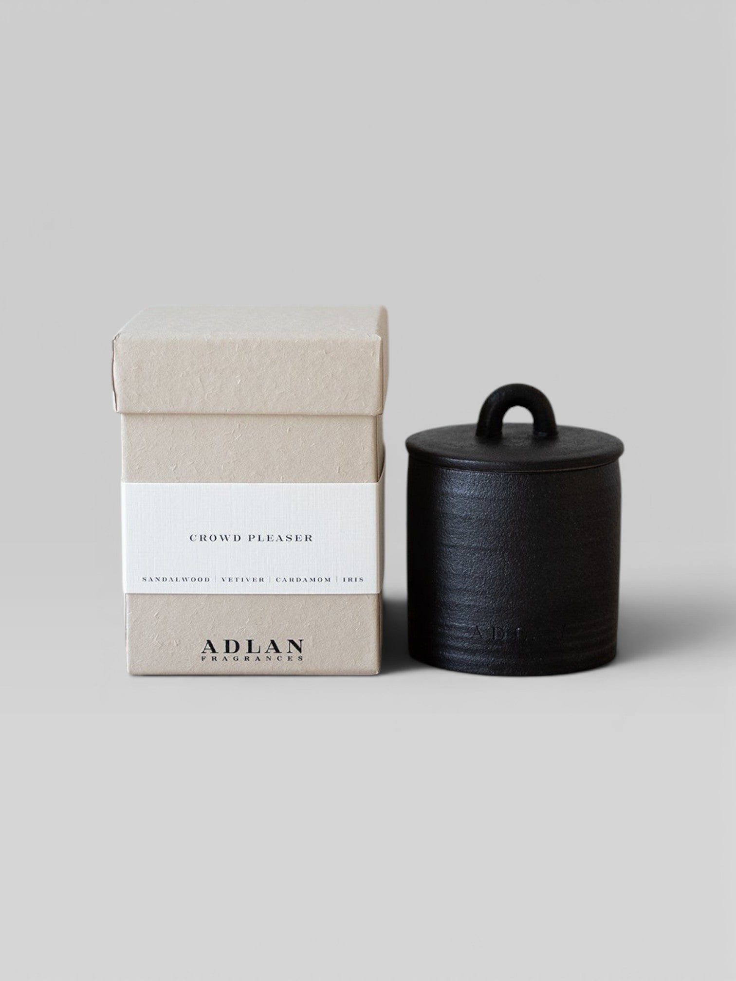 JONES + CO Crowd Pleaser petite candle in a black stoneware vessel next to its beige cardboard gift box.