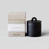 JONES + CO Mint Condition petite candle in a black stoneware vessel with a matching lid next to its beige gift box.