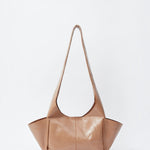 JONES + CO camel leather Tool Bag with a sculptural silhouette, fixed shoulder strap, and extended side pockets.