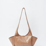 JONES + CO camel leather Tool Bag with a sculptural silhouette, fixed shoulder strap, and extended side pockets.
