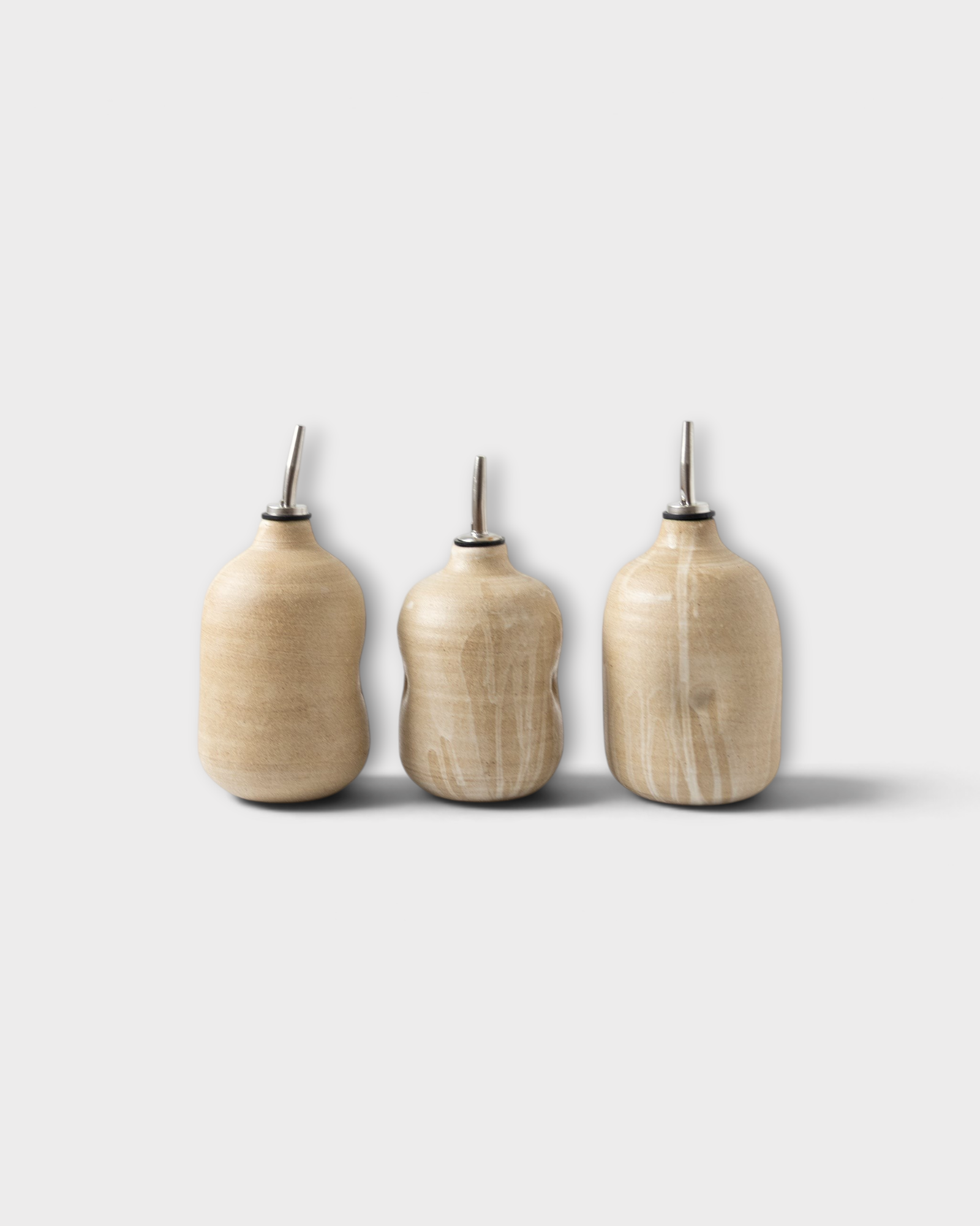 JONES + CO handmade ceramic olive oil cruets with metal spouts in a natural beige glaze finish.