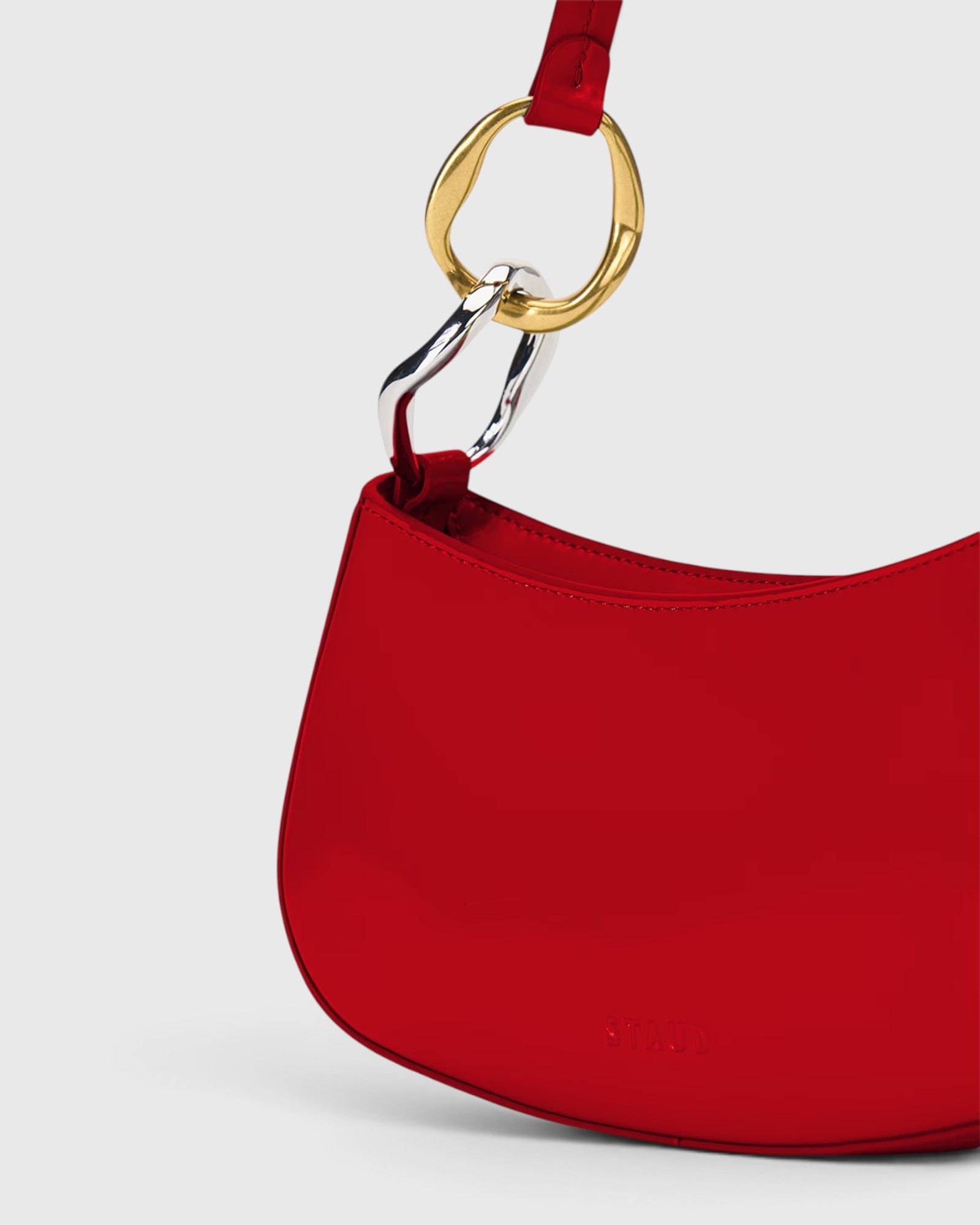 JONES + CO Ollie Bag in cherry-red polished leather with a crescent shape and mixed gold and silver strap hardware.