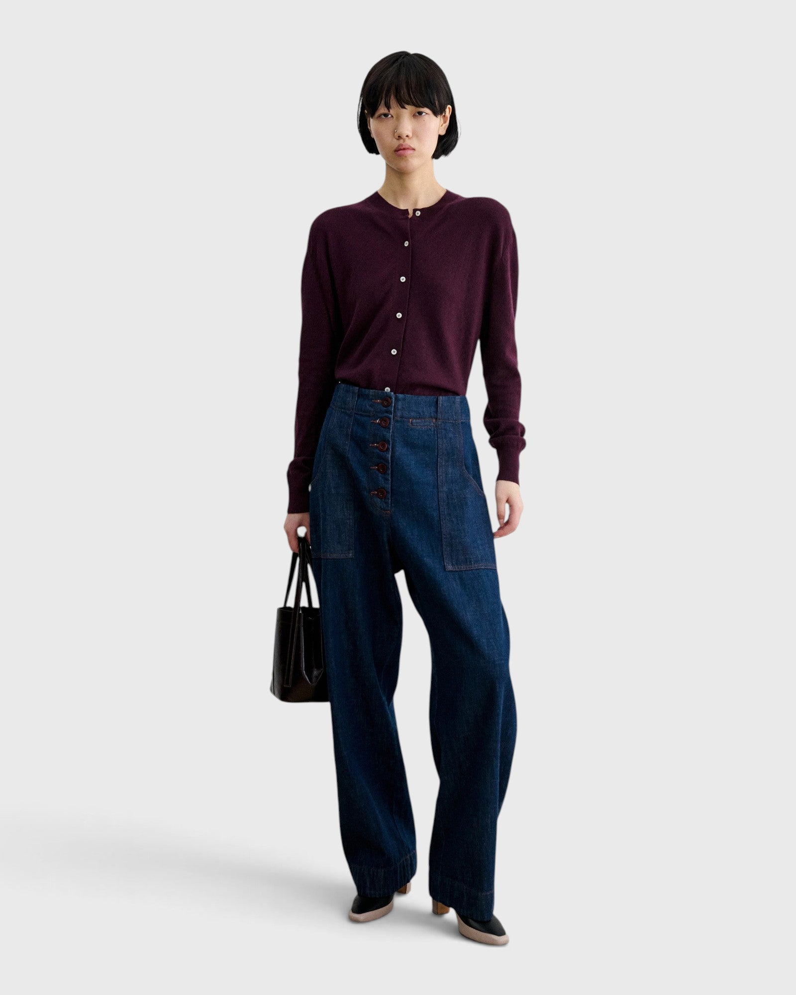 JONES + CO Chestnut lustre leather bucket bag with vertical paneling held by a model in a dark cardigan and jeans