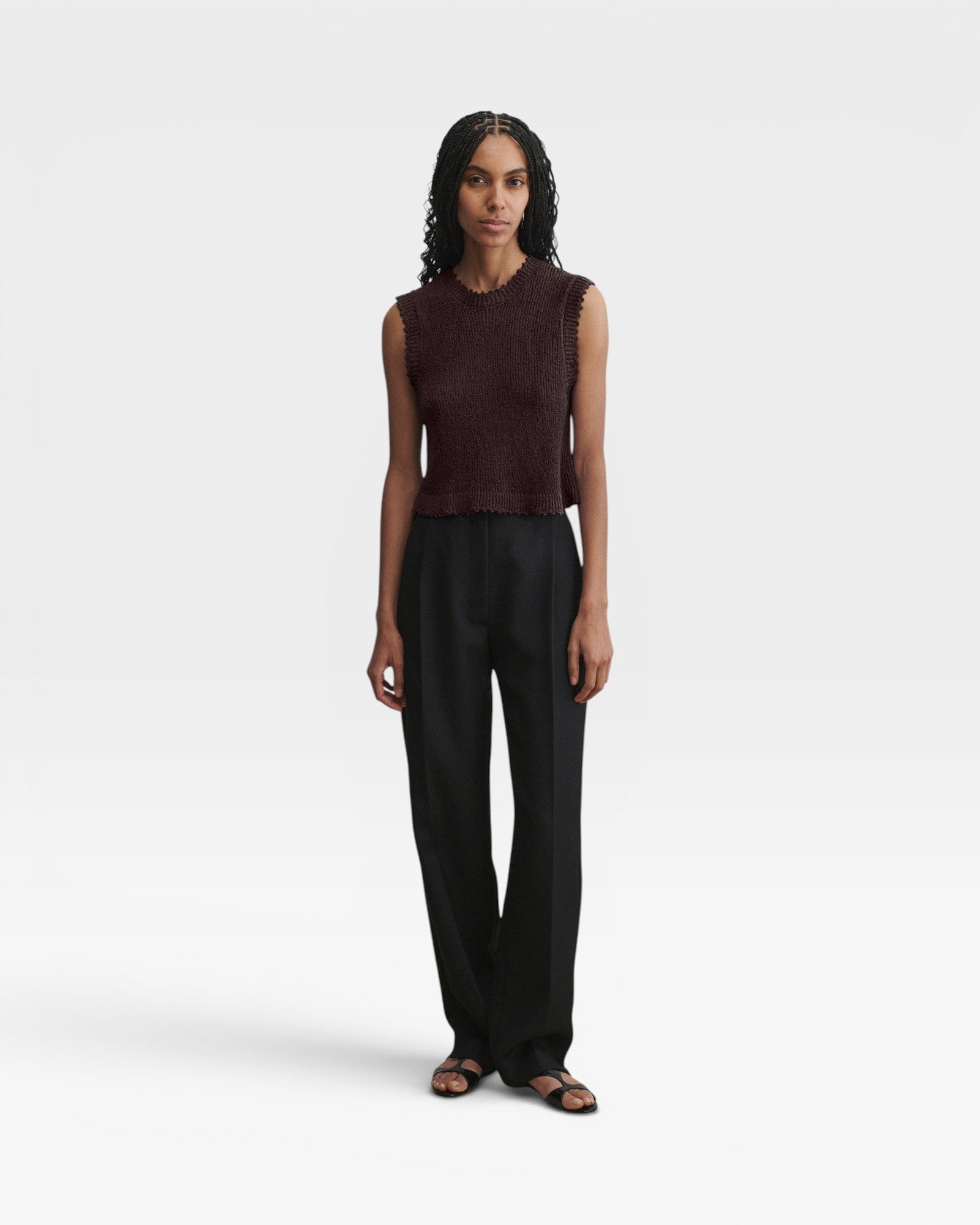 Model wearing a JONES + CO chocolate brown sleeveless cotton boucle crewneck top with picot trim and black trousers.