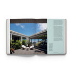 JONES + CO Courtyard Homes book open to a page showing a modern outdoor courtyard with white chairs and lush plants.