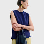 JONES + CO dark indigo lustre leather bucket bag with vertical paneling held by a woman in a navy blue knit vest.