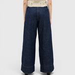 JONES + CO dark indigo wide-leg denim trousers with a high-waisted pleated fit, viewed from the back.