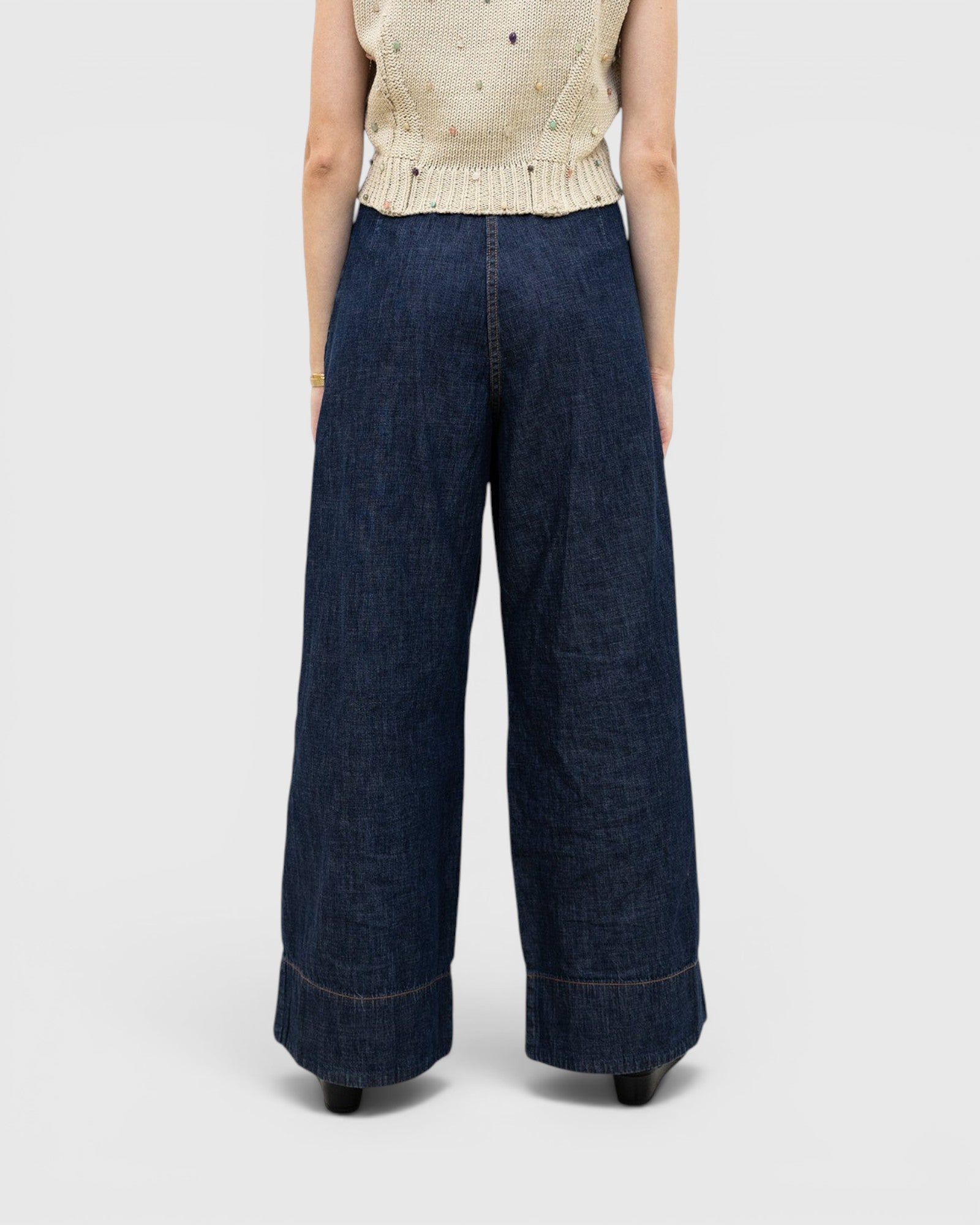 JONES + CO dark indigo wide-leg denim trousers with a high-waisted pleated fit, viewed from the back.