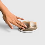 JONES + CO Erode Cardamom Vetiver soap with a unique sculpted shape resting on a white ceramic plate, touched by a hand.