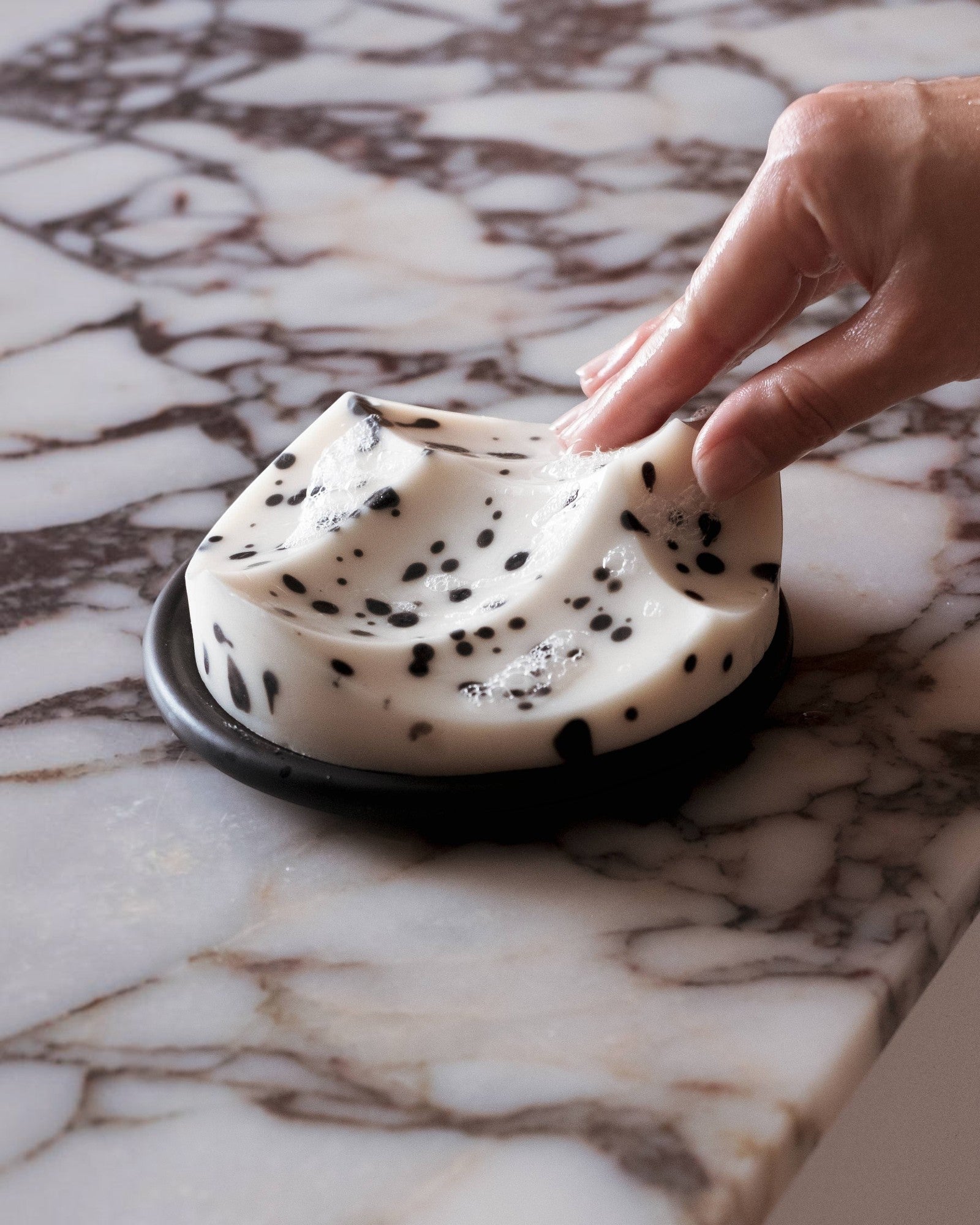 JONES + CO Erode Soap in White Grapefruit, a sculptural white bar with black botanical specks on a dark dish.