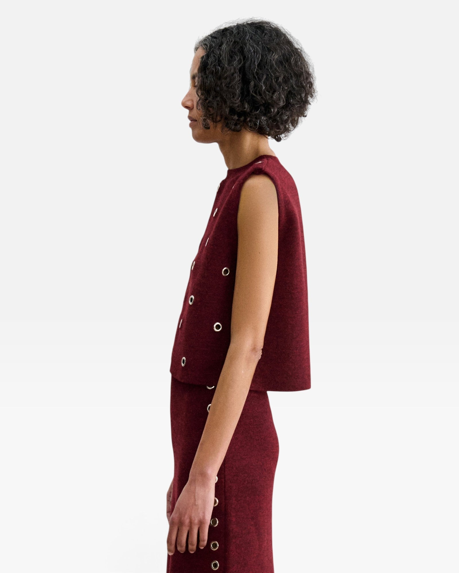 Model wearing JONES + CO garnet red baby alpaca Vega Vest with metallic eyelets in a boxy sleeveless silhouette