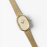 JONES + CO Jane Tethered watch with a gold oval case, champagne mother-of-pearl dial, and woven mesh bracelet.