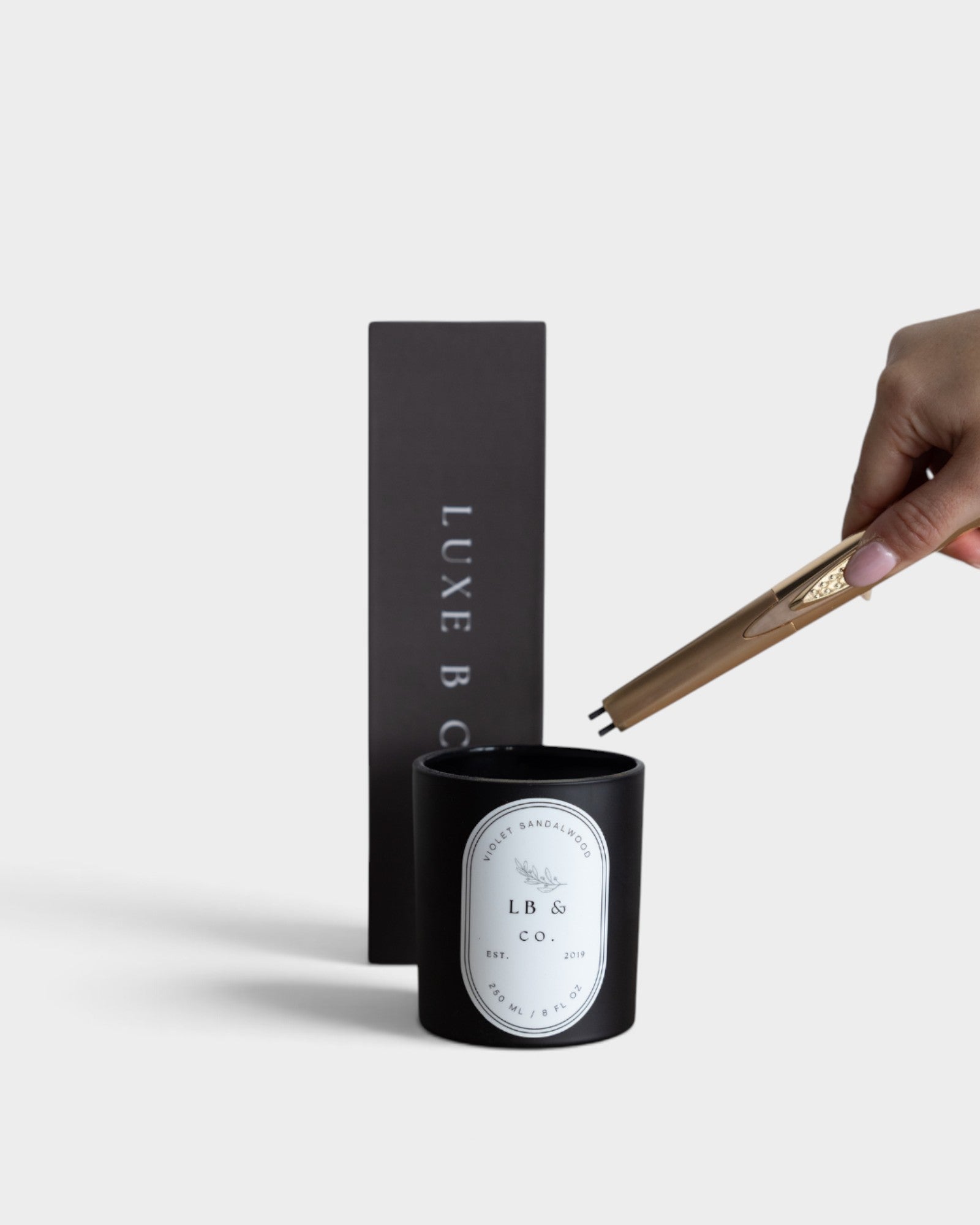 JONES + CO gold USB arc lighter igniting a black candle with a minimalist gift box in the background.