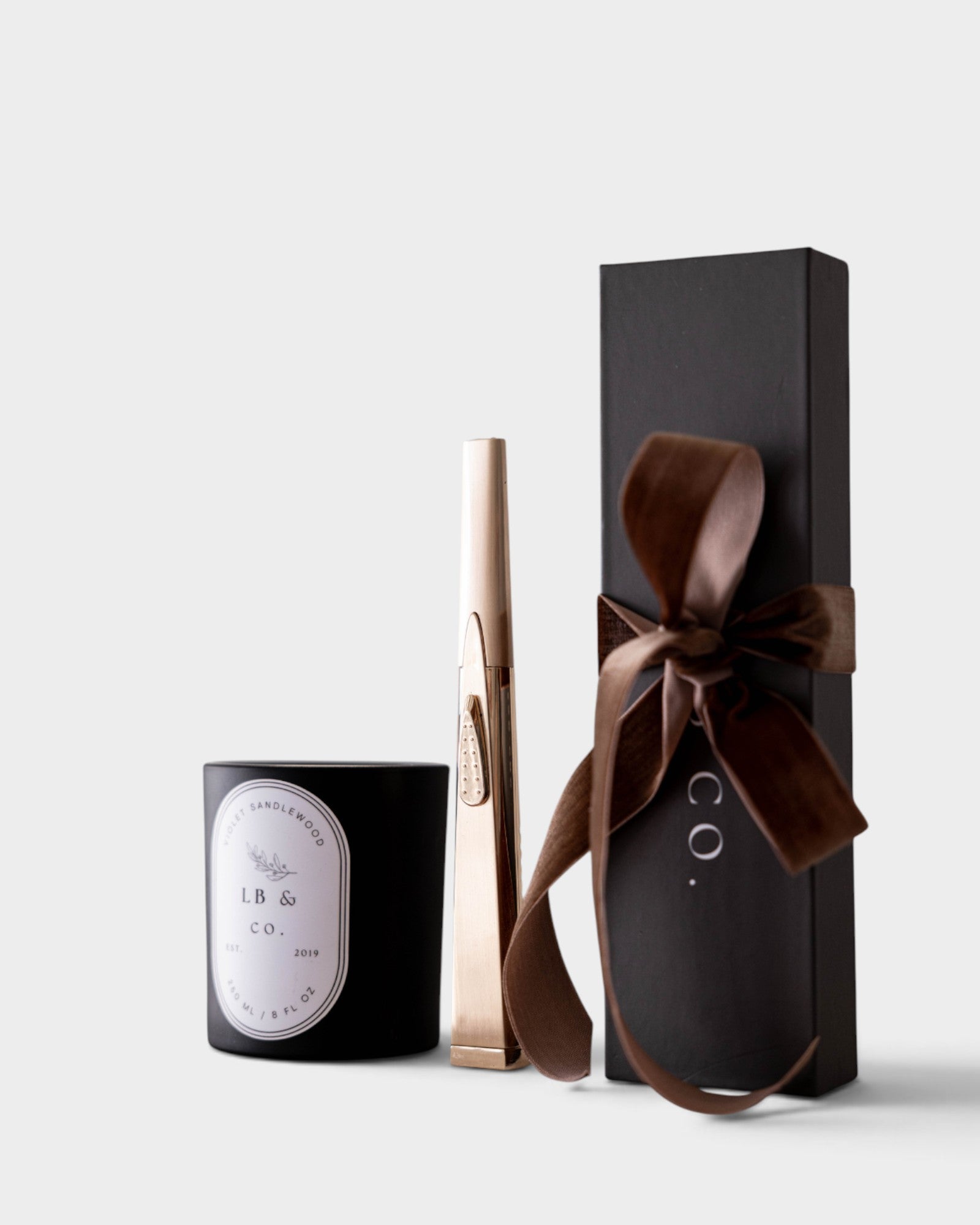 JONES + CO gold USB arc lighter standing next to a black candle and a gift box with a brown ribbon