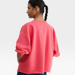 JONES + CO Fond crewneck sweatshirt in guava pink with drop shoulders and raw edge hem, worn by a model.