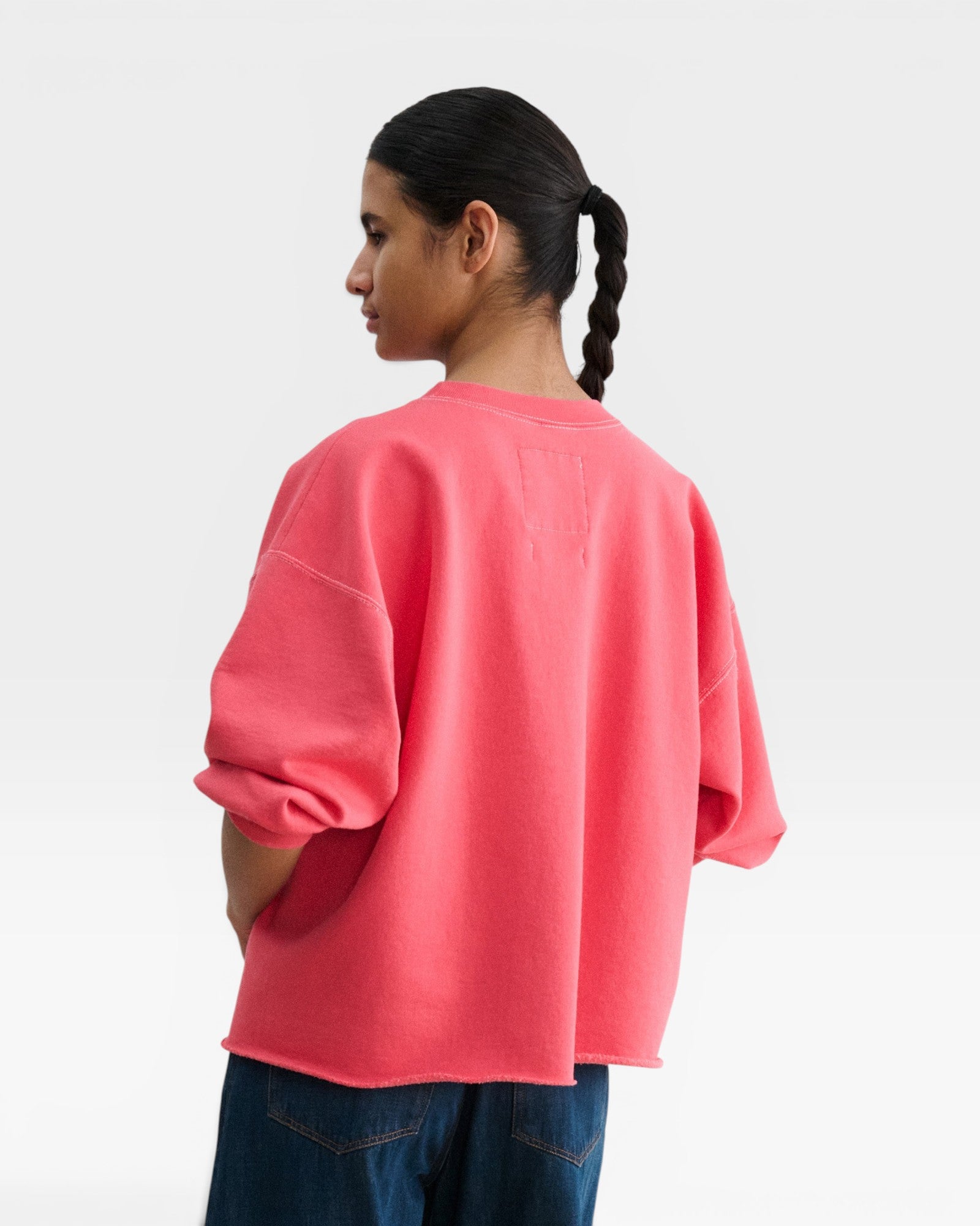 JONES + CO Fond crewneck sweatshirt in guava pink with drop shoulders and raw edge hem, worn by a model.