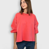 Model wearing a JONES + CO guava pink crewneck sweatshirt with drop shoulders and a raw edge hemline.
