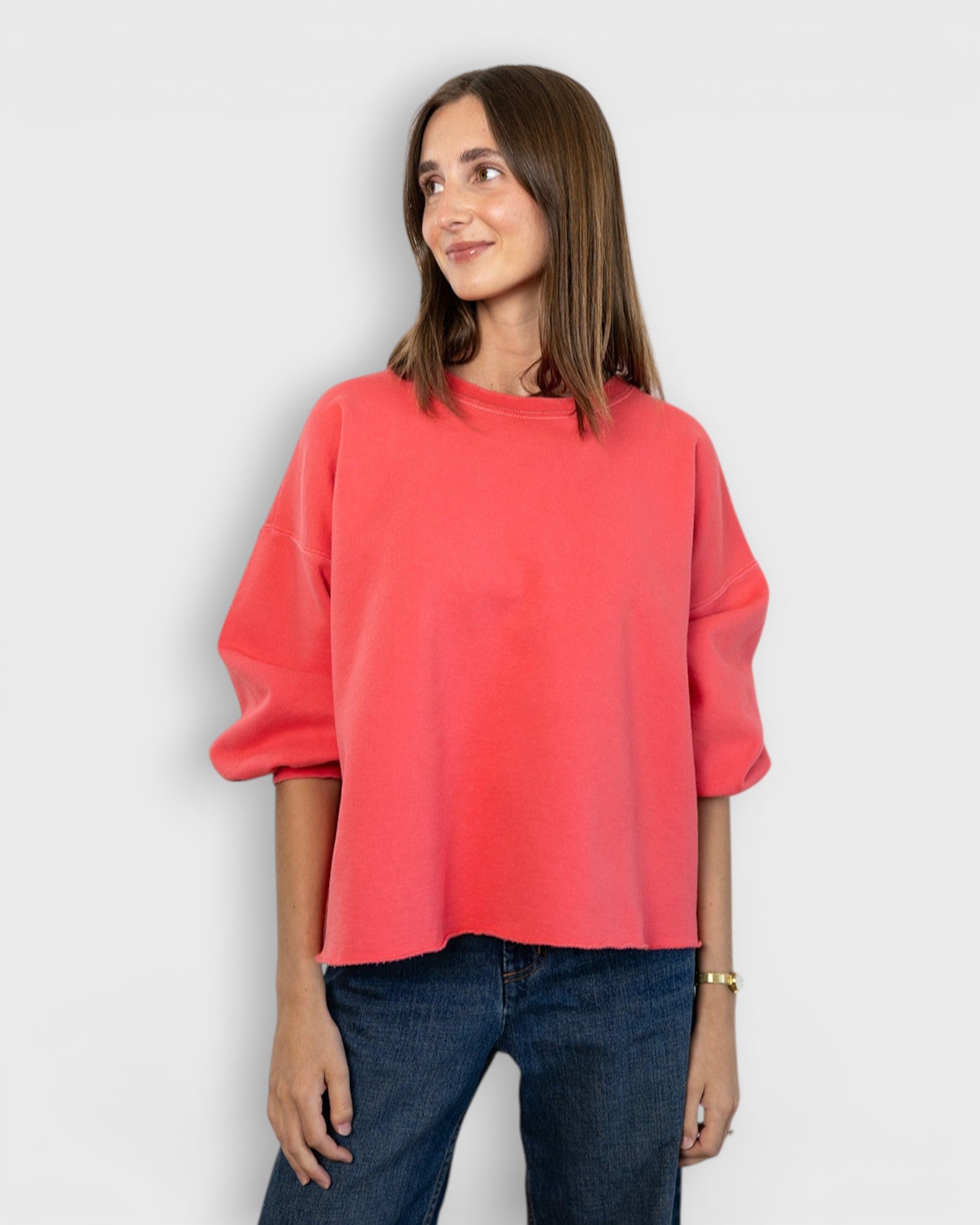 Model wearing a JONES + CO guava pink crewneck sweatshirt with drop shoulders and a raw edge hemline.