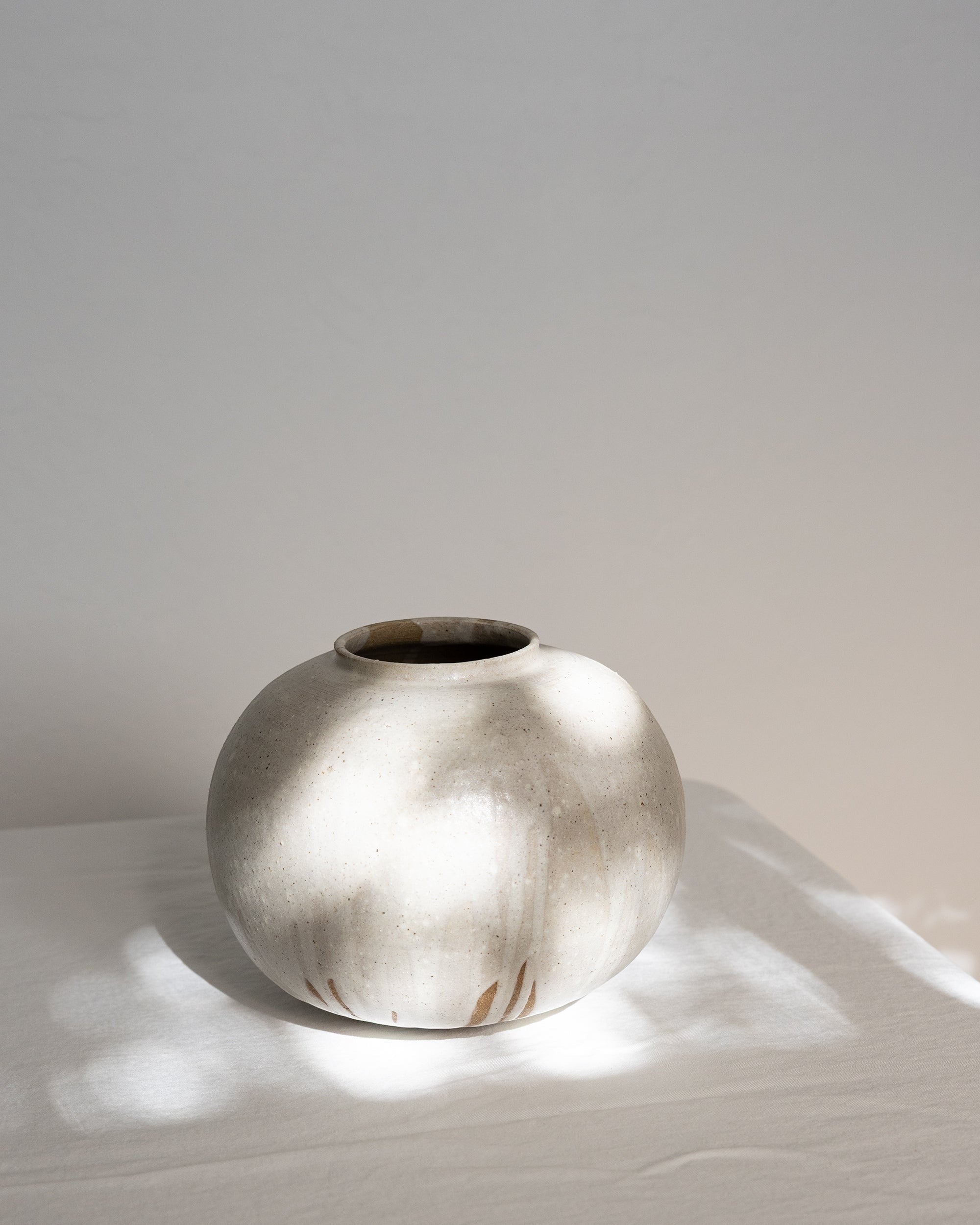 JONES + CO handthrown ceramic vase with a speckled off-white glaze and round sculptural shape on a white surface.