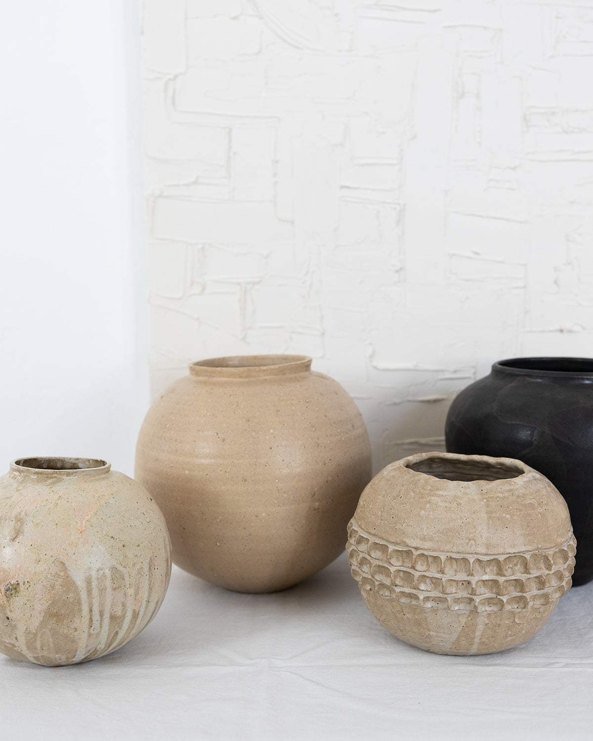 JONES + CO handthrown ceramic vases in neutral earth tones with textured and smooth finishes on a white surface.