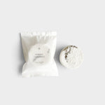 JONES + CO Hinoki shower steamer tablet with woody essential oils in white paper packaging on a neutral background