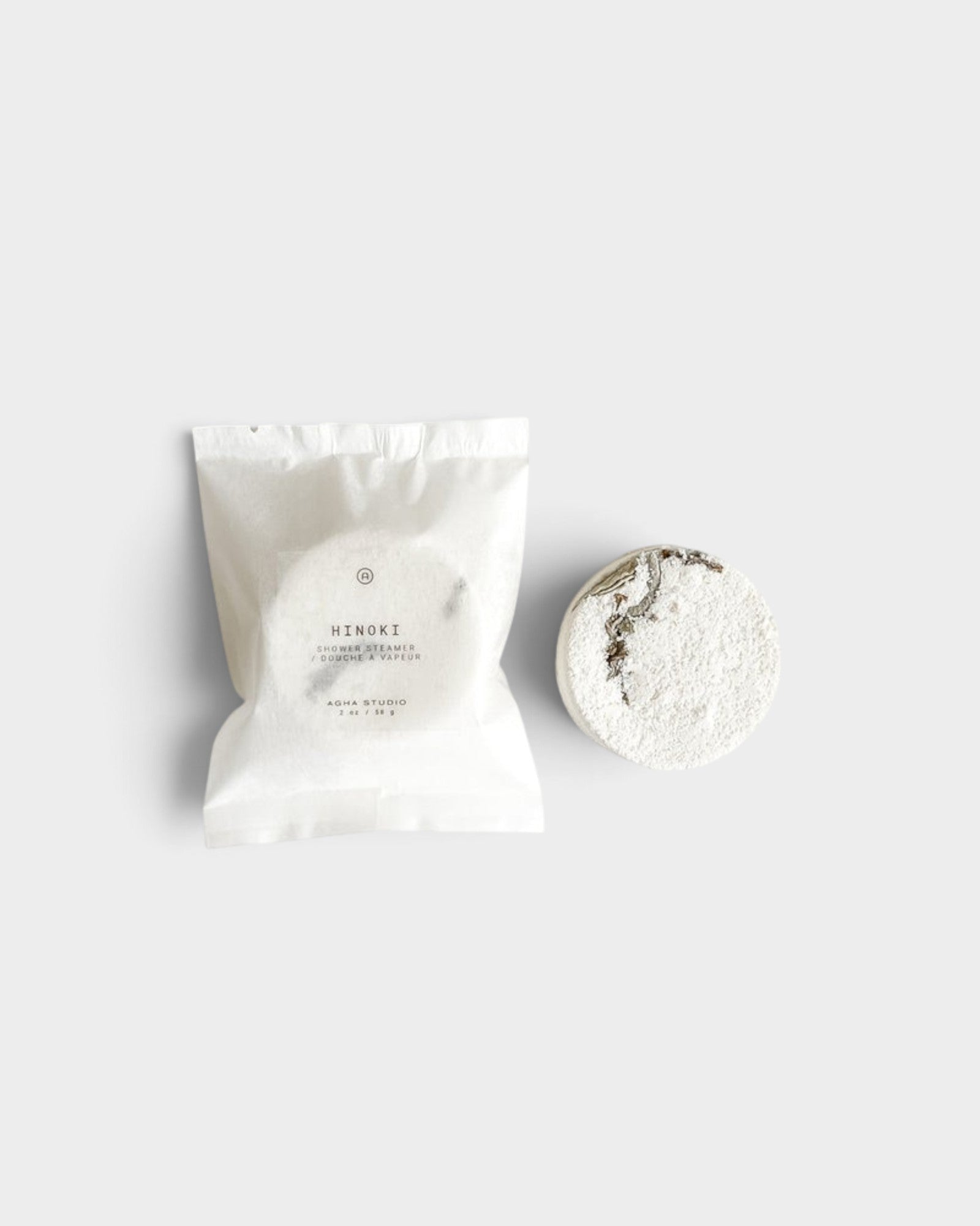 JONES + CO Hinoki shower steamer tablet with woody essential oils in white paper packaging on a neutral background