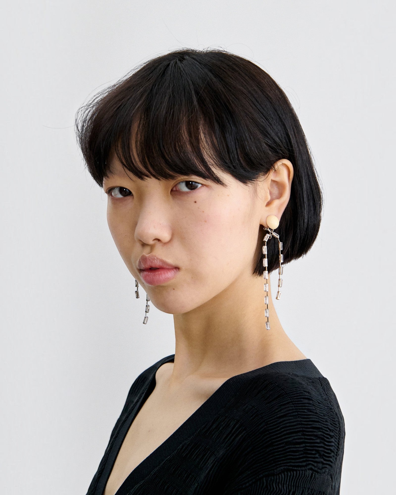 Model wearing JONES + CO ivory acrylic and brass draped baguette drop earrings against a plain white background.