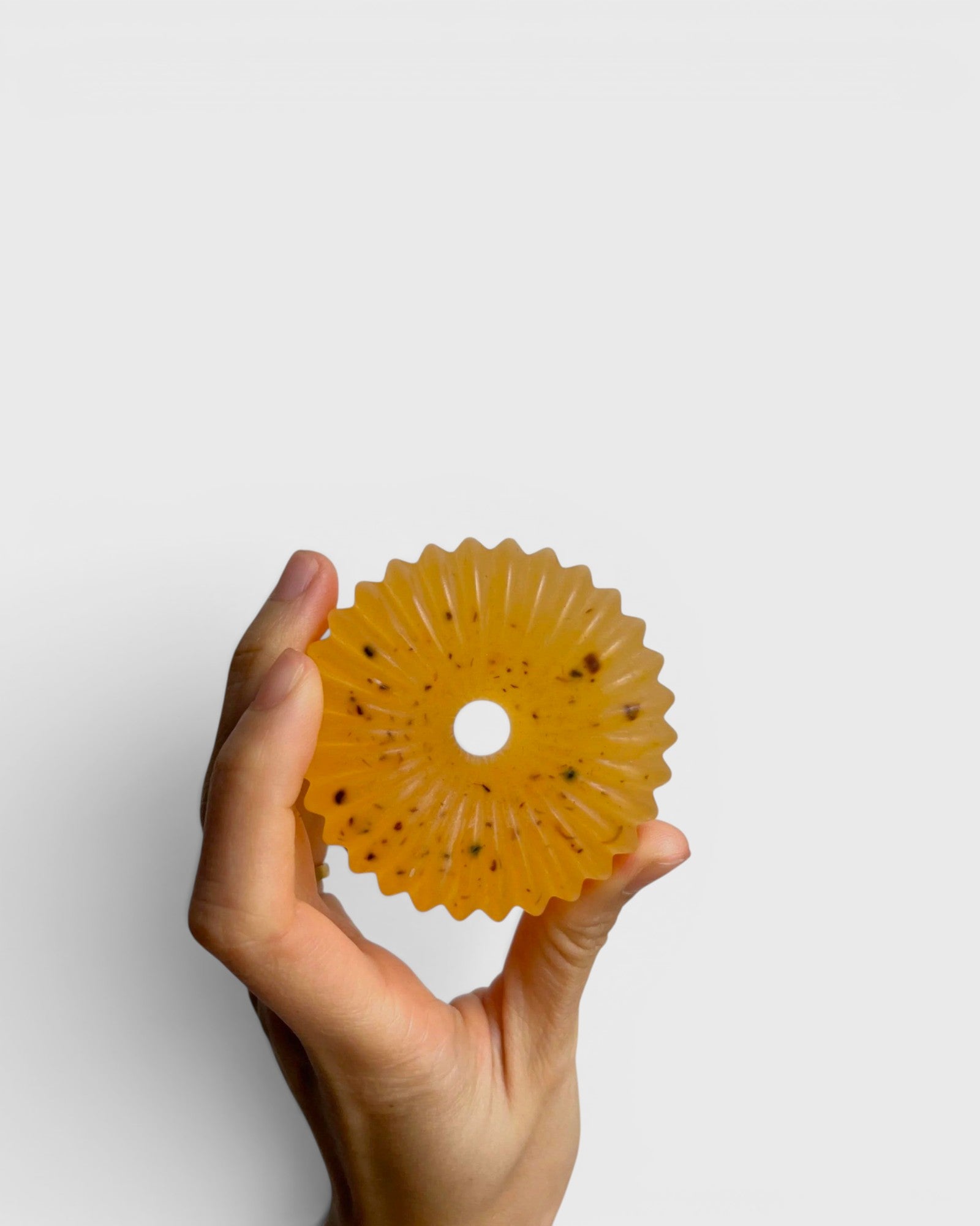 JONES + CO lülala basil and mandarin soap bar with calendula petals held in a hand against a white background.
