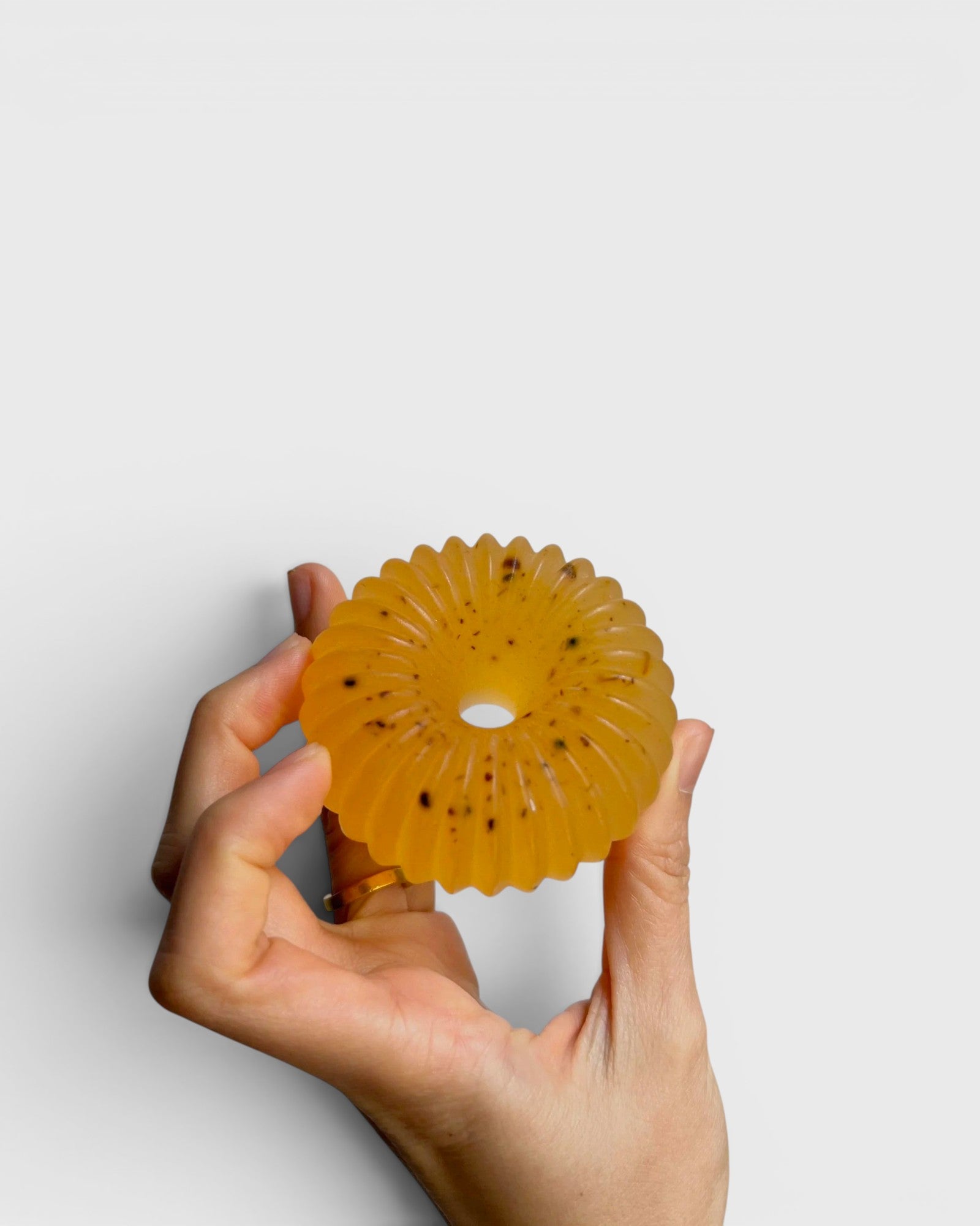 JONES + CO lülala soap bar in translucent orange with calendula petals, held in a hand against a white background.