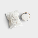 JONES + CO Menthol Eucalyptus shower steamer tablet with dried botanical petals next to its white paper packaging.