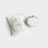 JONES + CO Menthol Eucalyptus shower steamer tablet with dried botanical petals next to its white paper packaging.