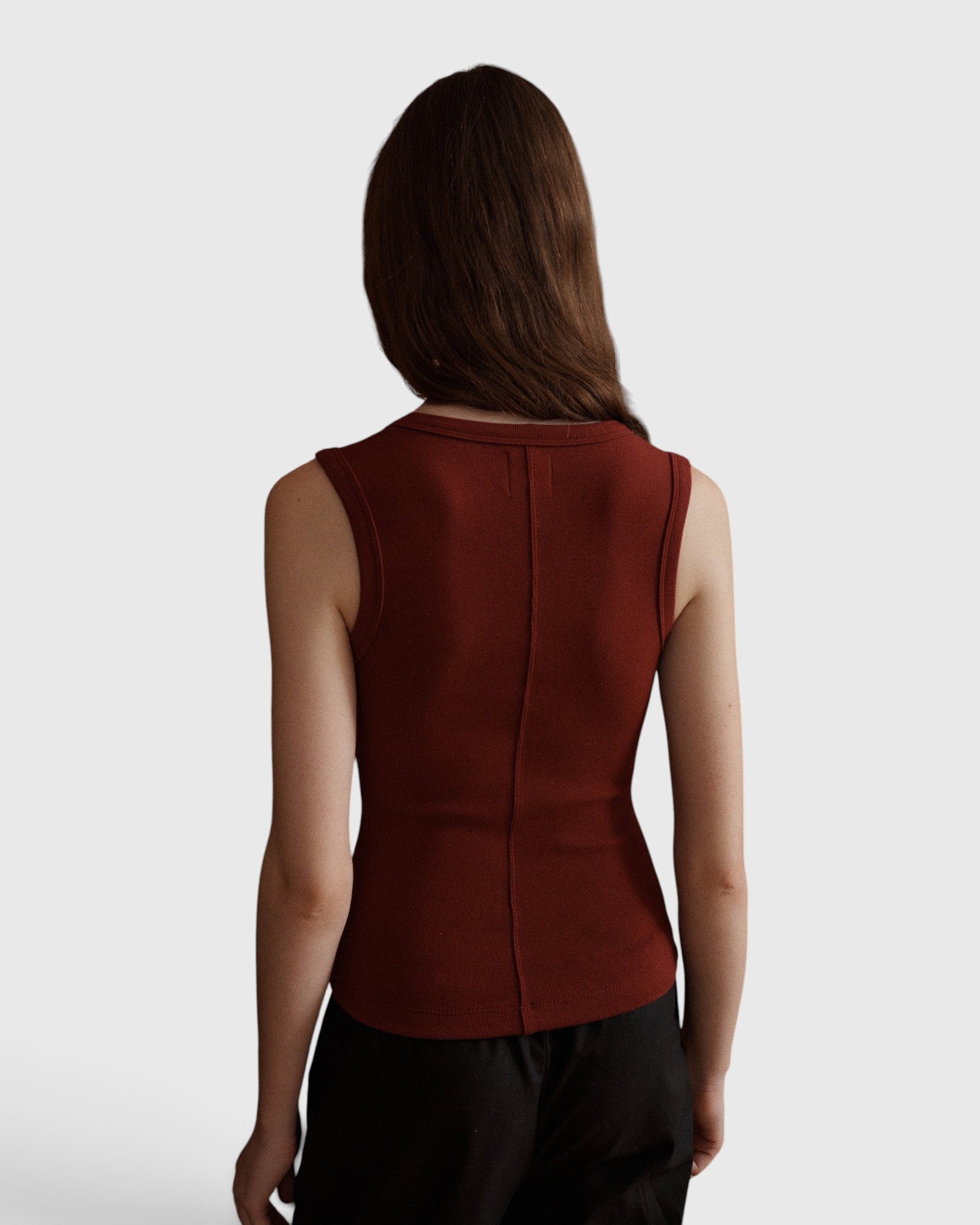 Back view of a model wearing the JONES + CO Kana Tank in merlot, featuring a ribbed knit and central seam detail.