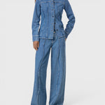Model wearing a JONES + CO mid-blue denim shirt with curved seams, pointed collar, and button-front closure.