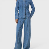 Model wearing a JONES + CO mid-blue denim shirt with curved seams, pointed collar, and button-front closure.
