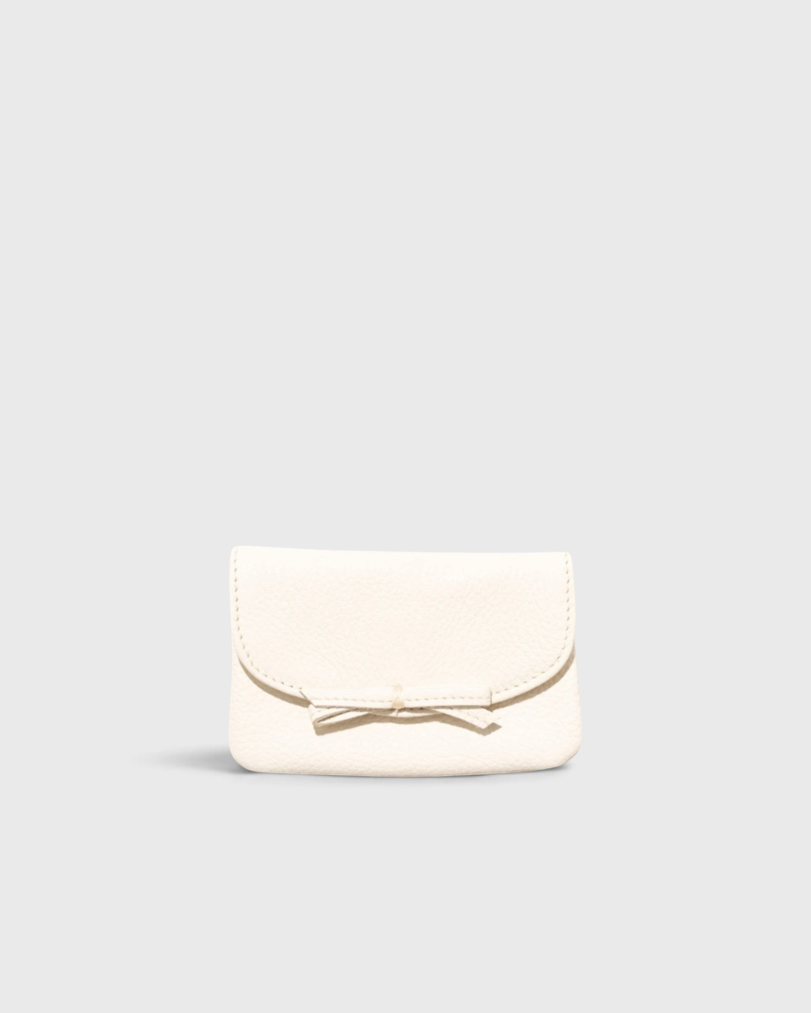 JONES + CO milk pebble grain leather petite case featuring a delicate knotted bow on the front flap