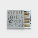JONES + CO Nue matchbox featuring a grey cover with an artistic alphabet illustration and white-tipped wooden matches.