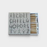 JONES + CO Nue matchbox featuring a grey cover with an artistic alphabet illustration and white-tipped wooden matches.