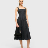 Model wearing a black midi dress and holding a JONES + CO Ollie Bag, a compact black leather shoulder bag.